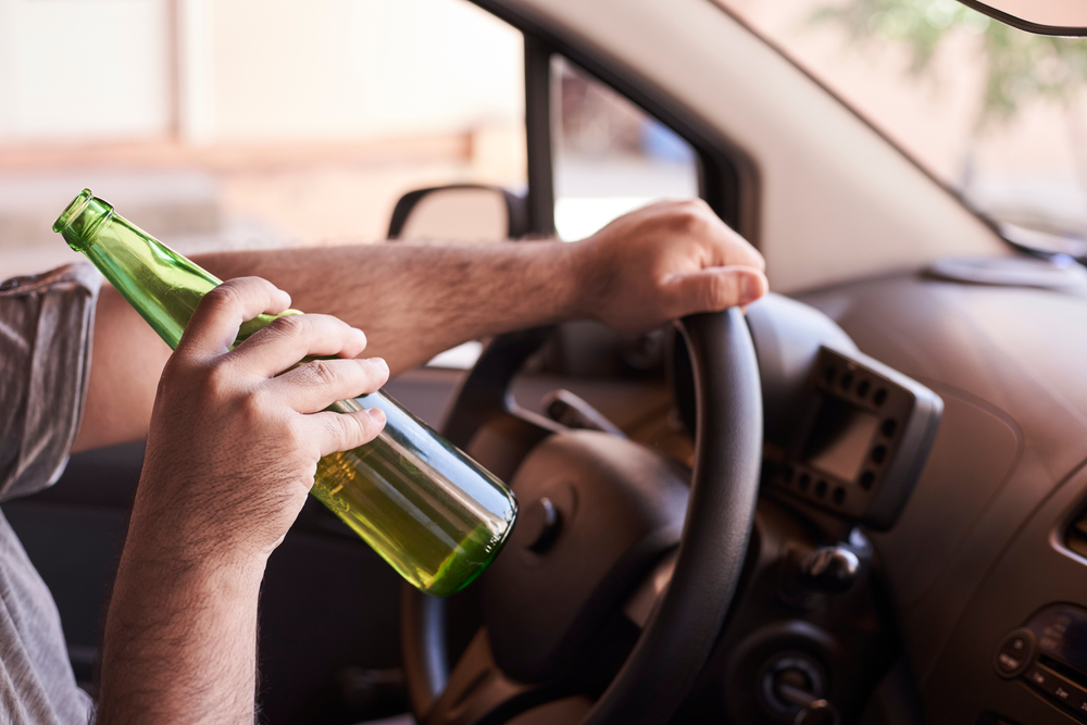 Driver holding a beer bottle behind the wheel, illustrating behavior that can lead to DUI stops in Lincoln