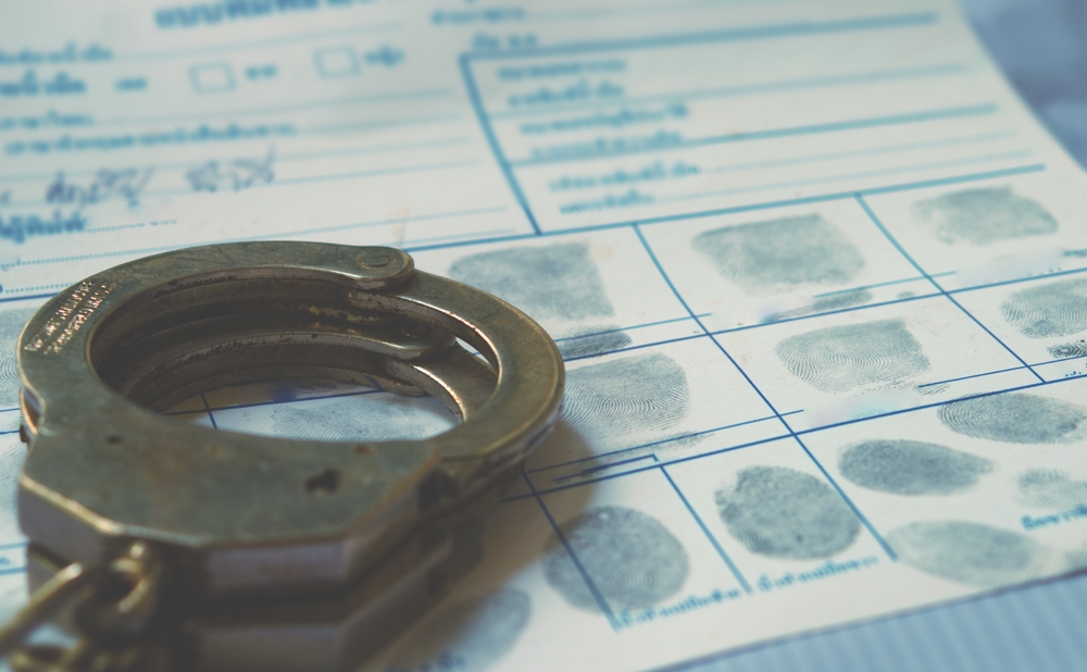 Stylized image of a criminal record with handcuffs on top of a fingerprint sheet