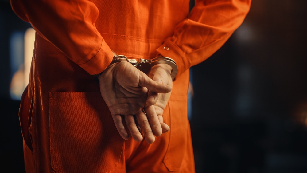 Close-up of man's hands in handcuffs wearing prison jumpsuit