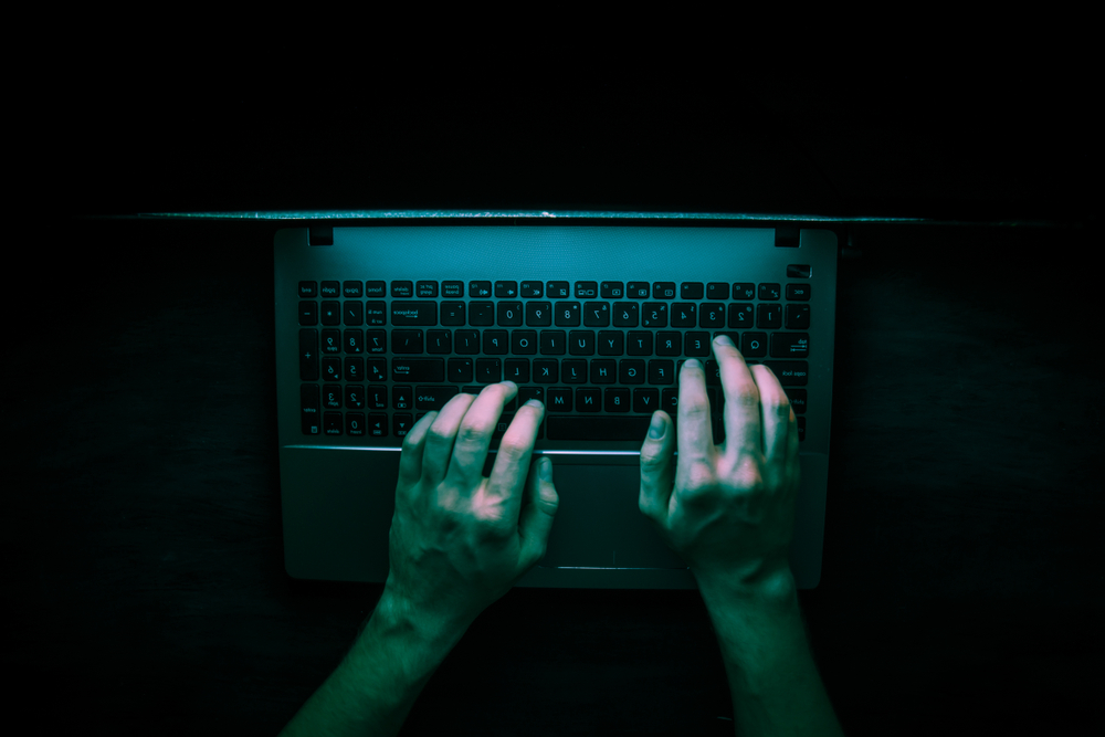 Stylized image of hands from above, using a laptop in the dark