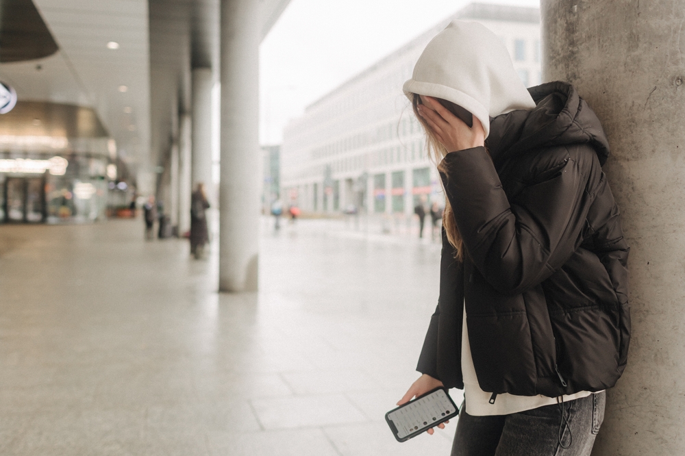 Teen victim of cyber bullying, crying in public while holding cell phone