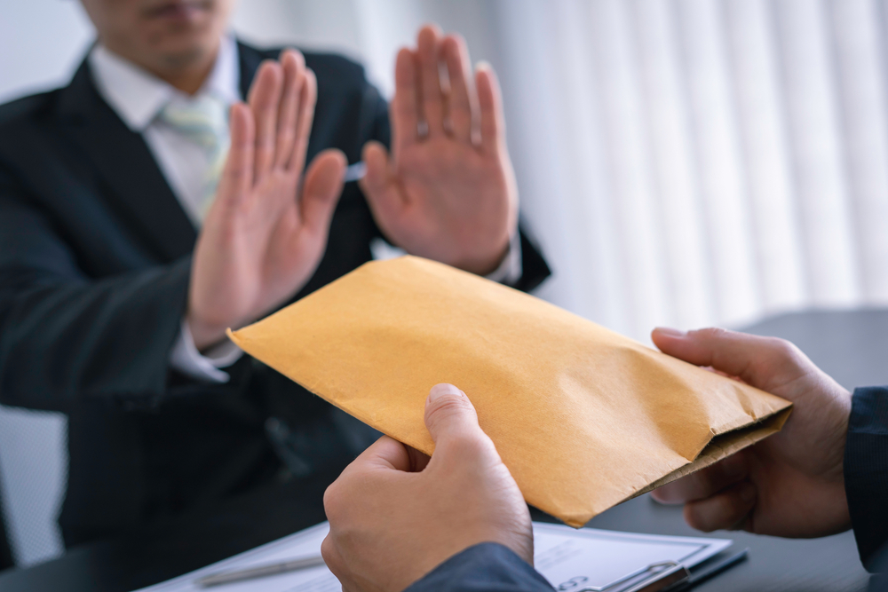 Man in suit refusing an unmarked manila envelope, insinuating a bribe
